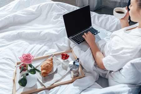 woman using laptop and having breakfast in bedの写真素材