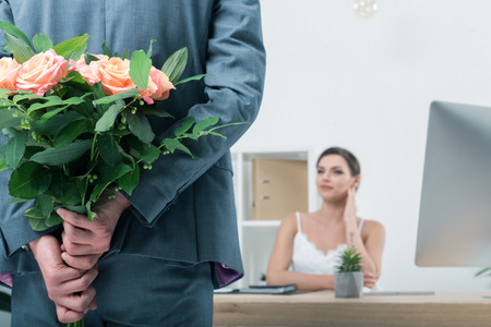 businessman holding bouquet of roses for his colleague sitting at workplaceの写真素材