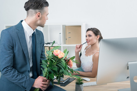 businessman presenting bouquet of roses to his colleague at workplaceの写真素材