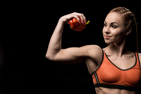sporty girl holding bell pepper solated on blackの写真素材