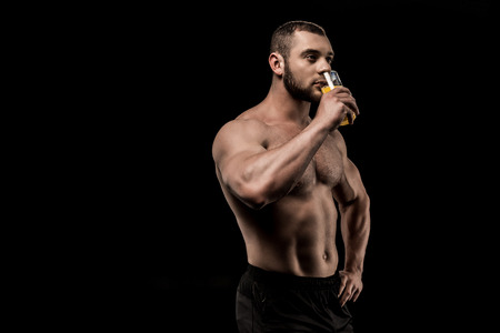 sportive shirtless man drinking juice isolated on blackの写真素材