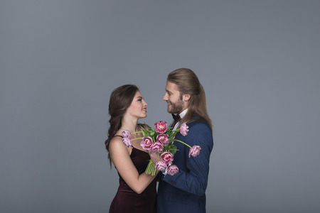 sweethearts in evening outfit holding bouquet of peonies and looking on each otherの写真素材