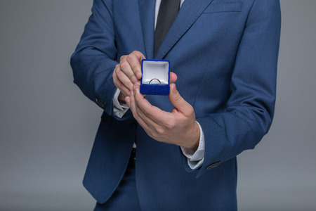 stylish man in suit holding golden wedding ring in box