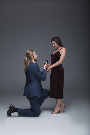 man in tuxedo making marriage proposal to his girlfriend while standing on one kneeの写真素材