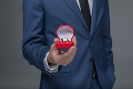 stylish man in suit holding golden wedding rings in box