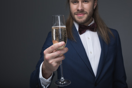 man in tuxedo holding glass with champagne and looking at cameraの写真素材