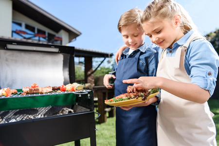 children testing fresh meat just cooked on barbecue grill outdoorsの写真素材