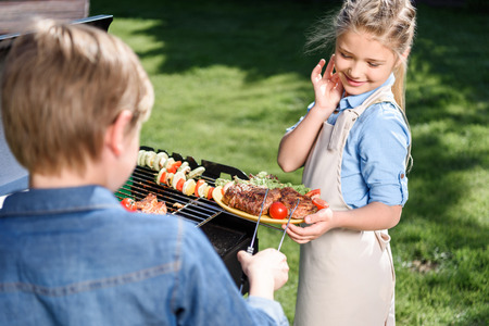 kids preparing meat and vegetables on barbecue grill outdoorsの写真素材