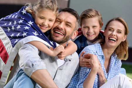 Happy family with american flag hugging outdoorsの写真素材