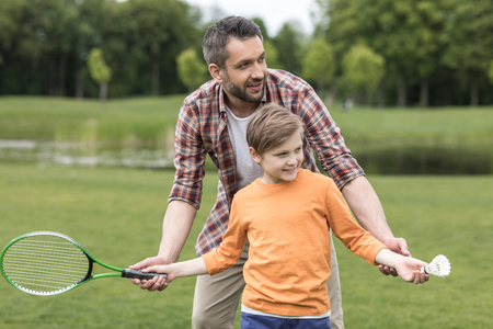 father teaching little son playing badminton outdoorsの写真素材