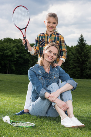 mother and daughter resting on green lawn after play badmintonの写真素材