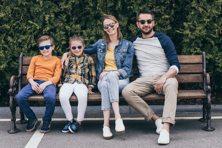 family in sunglasses sitting together on bench at parkの写真素材