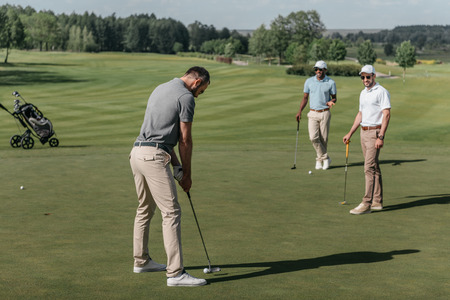 friends playing golf together on green at daytimeの写真素材