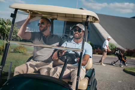 smiling man riding golf cart with friend sitting near by