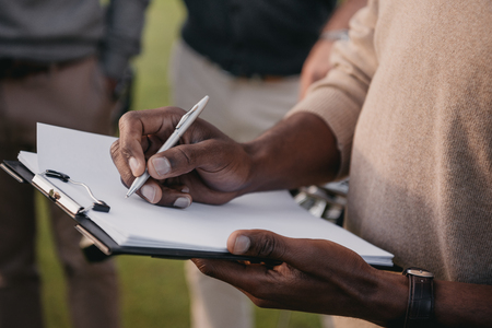 cropped view of african american man writing something on paper in clipboardの写真素材