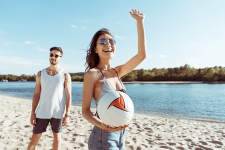 woman with volleyball ball in hand waving to someone on beachの写真素材