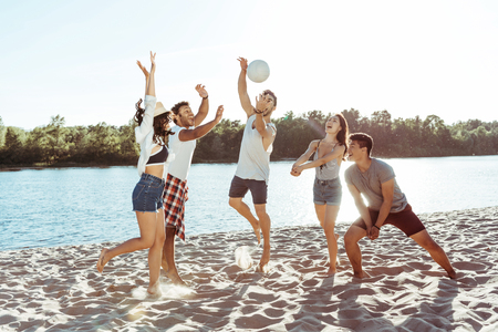 young friends playing volleyball on sandy beach at daytime