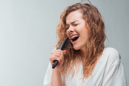 blonde woman singing with hair comb, isolated on greyの写真素材