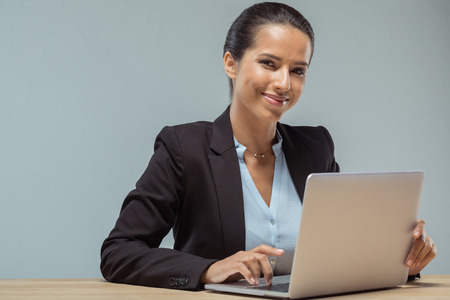 smiling businesswoman looking at camera while typing on laptopの写真素材