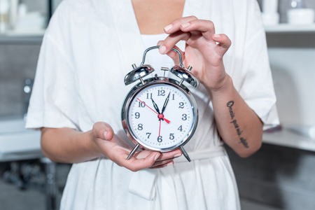 woman in bathrobe holding alarm clock indoorsの写真素材