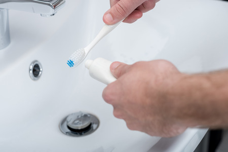 man applying toothpaste on toothbrush in bathroomの写真素材