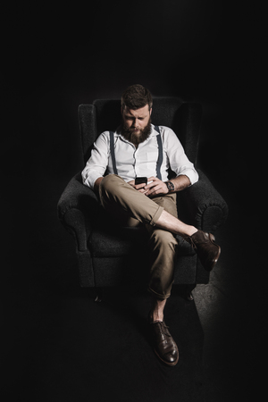 fashionable man using smartphone while sitting in armchairの写真素材