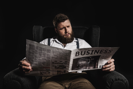 fashionable man reading business newspaper while sitting in armchairの写真素材