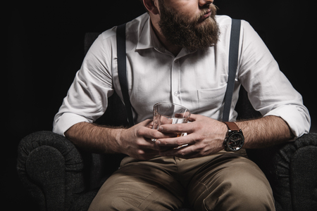 cropped view of stylish man in white shirt and suspenders holding whisky glassの写真素材