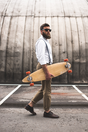 fashionable man in sunglasses walking with longboard on parking placeの写真素材