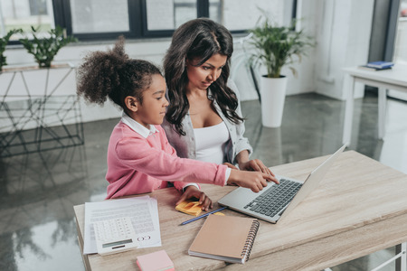 businesswoman typing on laptop with daughter near byの写真素材