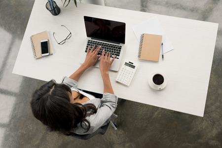 businesswoman typing on laptop while sitting at workplace in officeの写真素材