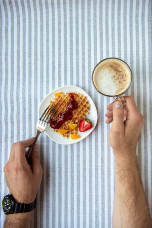 person eating fresh homemade waffles and drinking coffee at breakfastの写真素材