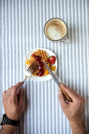 person eating fresh homemade waffles and drinking coffee at breakfastの写真素材