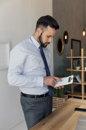 concentrated businessman using calculator while standing at workplaceの写真素材