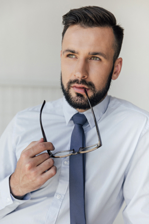 pensive businessman with eyeglasses in hand looking awayの写真素材
