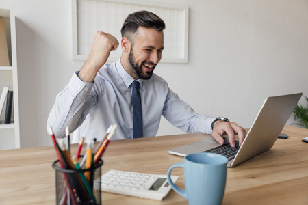 happy businessman typing on laptop in modern officeの写真素材