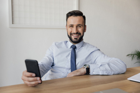 smiling businessman using smartphone while sitting at workplaceの写真素材