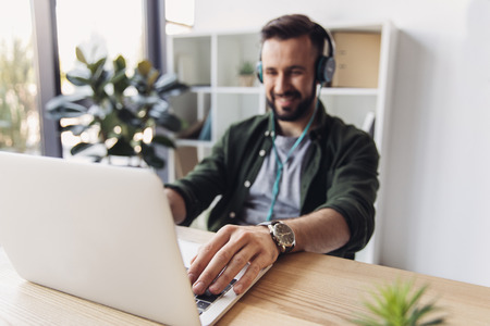 bearded man in headphones using laptop while sitting at tableの写真素材