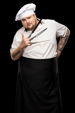 young chef in hat and apron holding knives and showing thumb upの写真素材