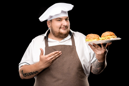 portrait of smiling cooker pointing at plate with burgersの写真素材