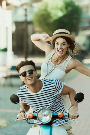young stylish couple having fun and riding scooter in cityの写真素材