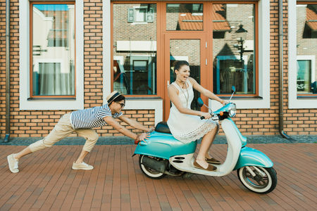 man helping excited woman riding retro scooterの写真素材