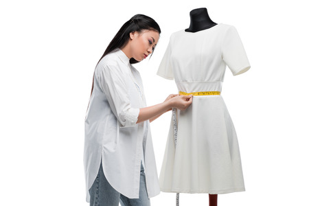attractive concentrated asian tailor measuring stylish white dress on dummyの写真素材