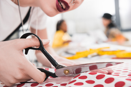 young dressmaker cutting polka dot fabric with scissorsの写真素材