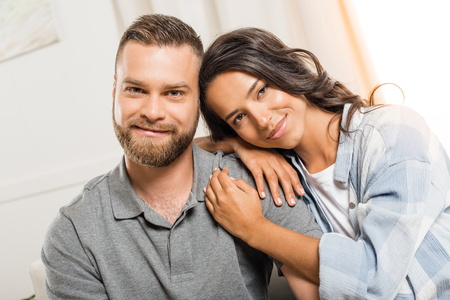 smiling couple hugging and looking at camera at homeの写真素材