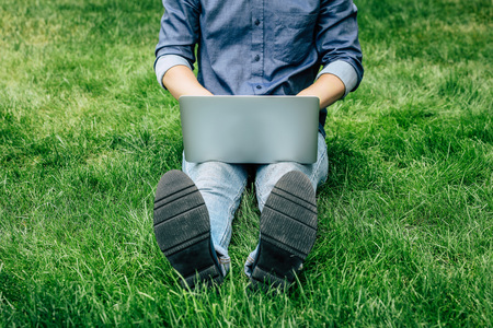 Low section of young man using laptop while resting on green grassの写真素材