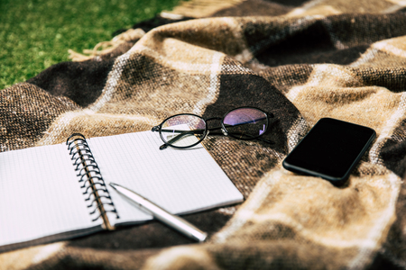 close up view of blank notebook, smartphone and eyeglasses on blanketの写真素材