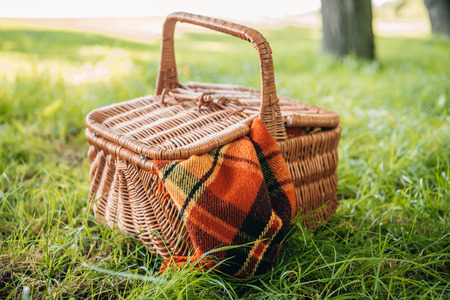 Close-up view of wicker picnic basket with plaid on green grass in parkの写真素材