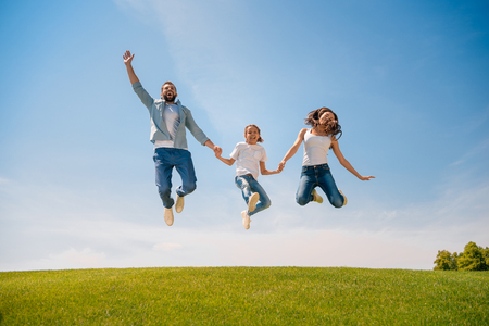 young family with one child holding hands and jumping on meadowの写真素材