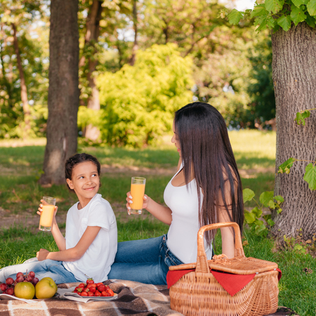 happy mother and daughter drinking juice and smiling each other at picnicの写真素材